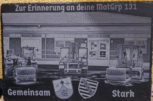 Gravierte Gedenktafel mit Text und Symbolen zur Erinnerung an die MatGrp 131.