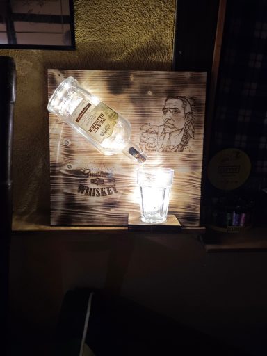 Ein Holzbrett mit einer Flasche und einem Glas, beleuchtet von unten.