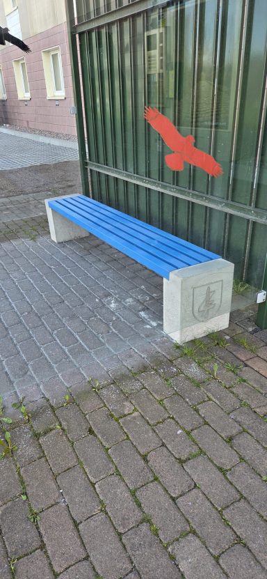 Blaue Bank vor einer grünen Wand mit einem roten Vogelsymbol.